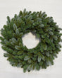 A circular green pine wreath with a frosted, dusty blue-gray finish, photographed from directly above on a light off-white background.