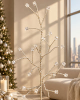 A decorative branch-style silk stem with multiple clear faceted square crystals attached to a thin gold-toned branch structure, held by a hand against a dark olive-gray wall.